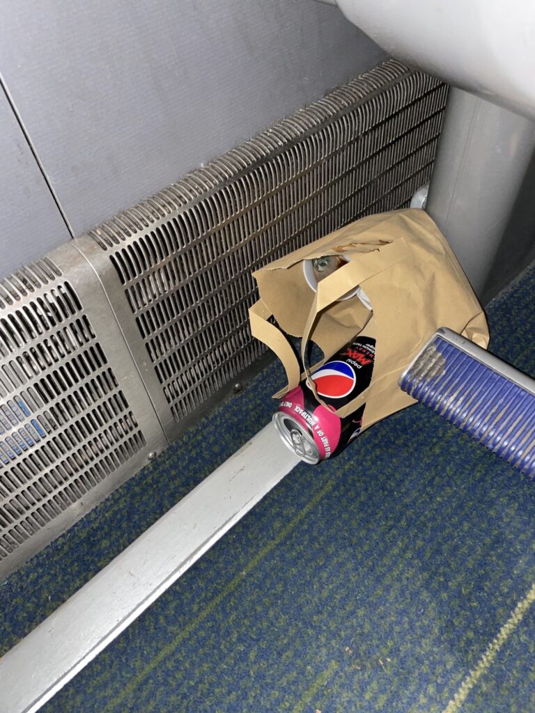 Some garbage is stuffed in a brown paper bag under the train seat. 