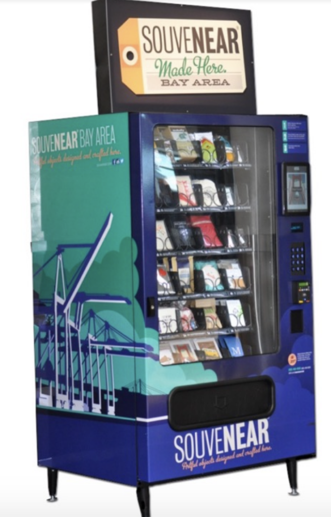 SouveNEAR Machine is a normal looking vending machine with a large window to see the selection and green and blue decorative exterior panels.