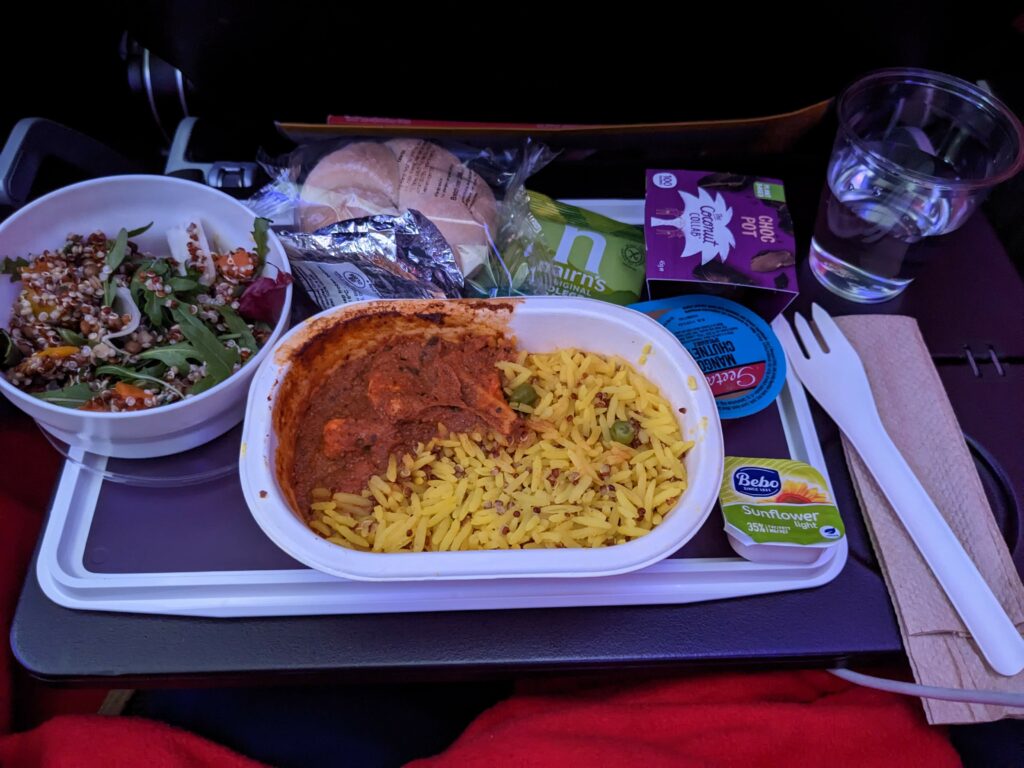 An Indian lunch with meat and rice, a side salad, plus a roll, beverage and dessert.