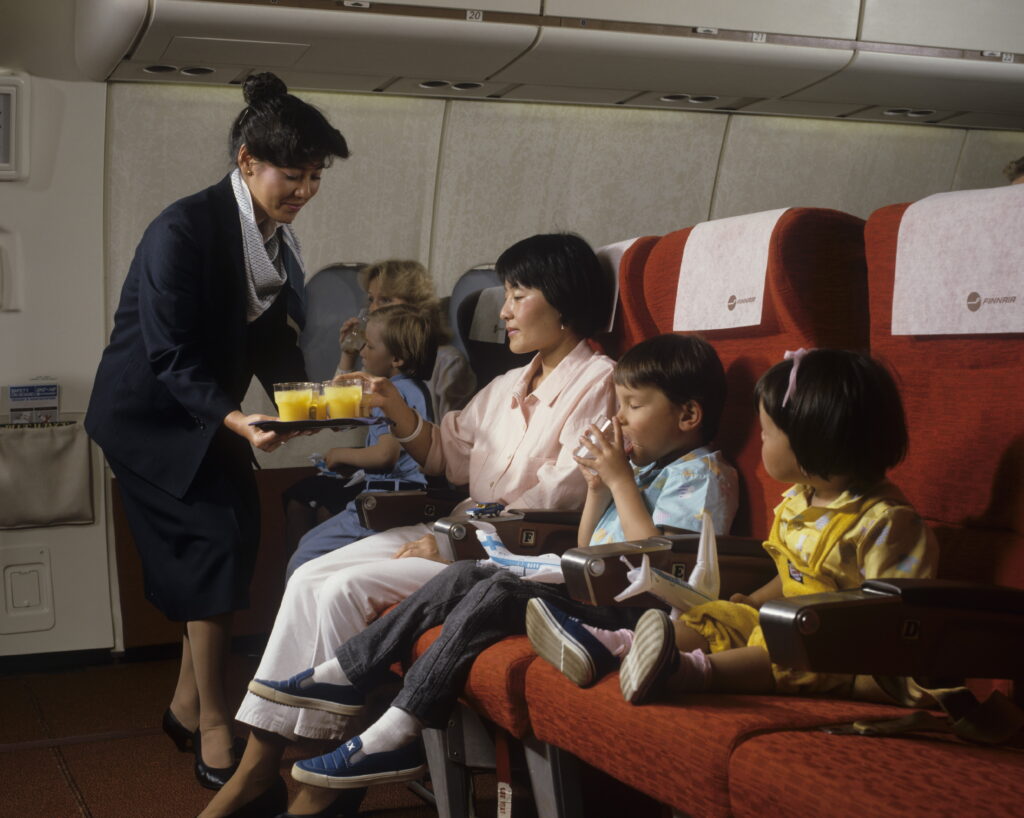 Passengers on a Finnair flight to Japan from decades ago. A flight attendant serves them beverages.