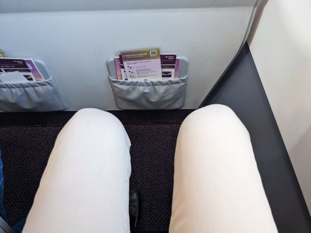 First row Premium Economy legroom shows a mans knees a distance away from the bulkhead in front of him.