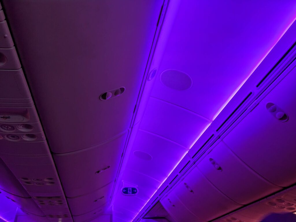 Light purple mood lighting is shown throughout the Virgin Atlantic aircraft. This image focuses on the LEDs above the overhead bins.