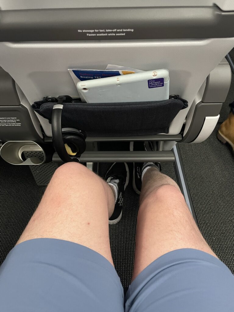 A man's knees are shown close to the seat in front of him in premium economy.