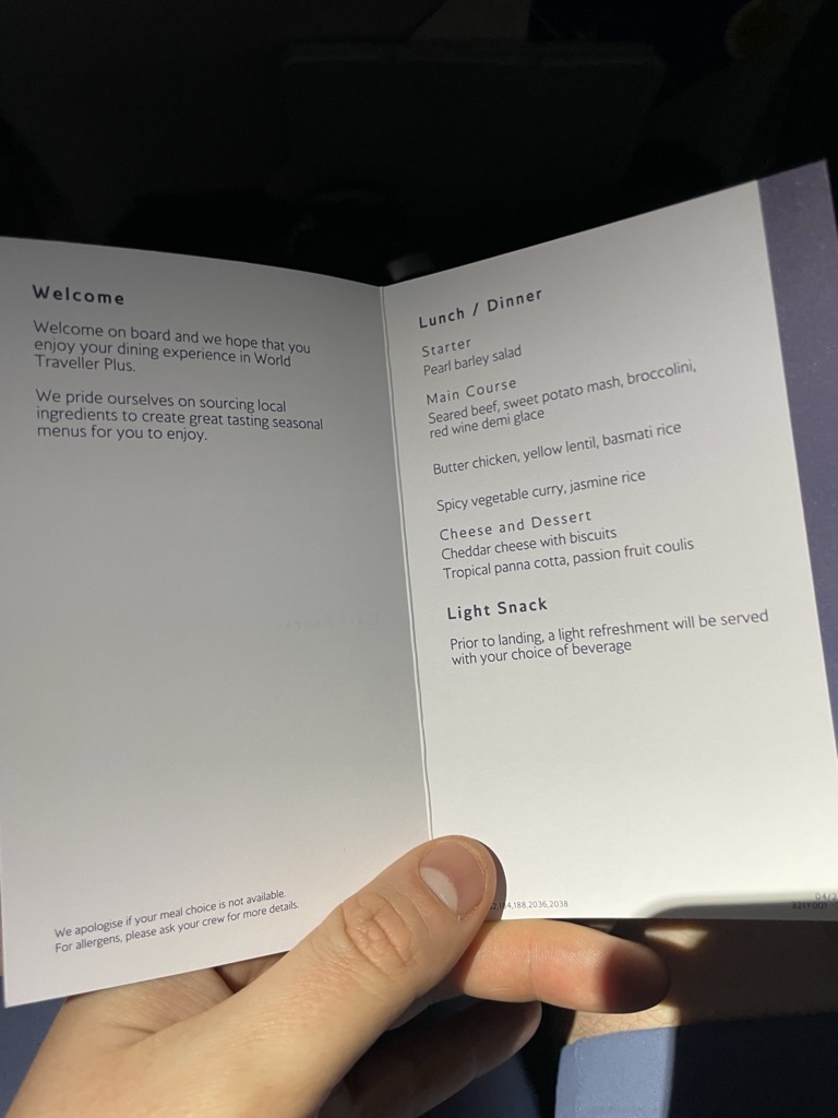 A hand is holding up the menu for premium economy dining. 