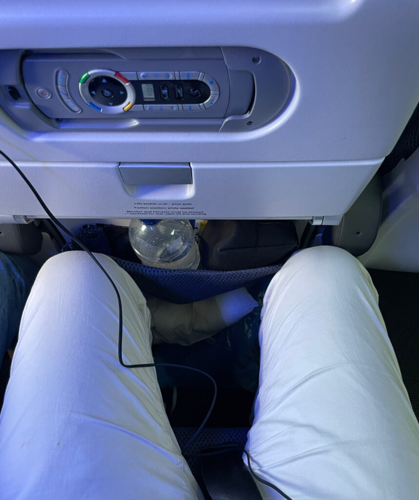 The author's legs in relation to the seatback in front of him. He has roughly two inches of extra space before meeting the seatback with his knees. He is quite a tall person. 