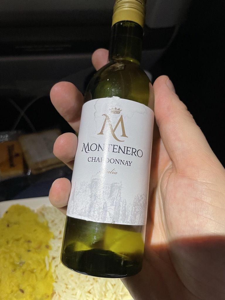 A hand is holding up a small bottle of white wine. 