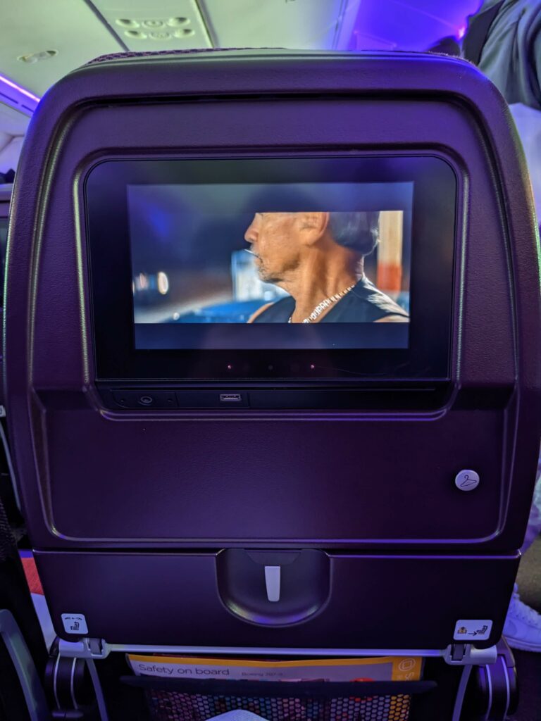 Virgin Atlantic seatback, in purple, with embedded IFE playing a movie.