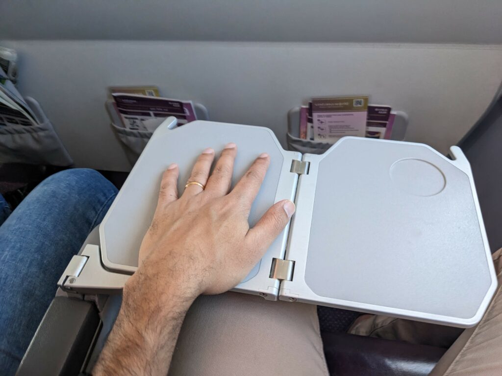 The author's hand sits atop the bi-fold tray table in Premium Economy on Vistara's A320neo.