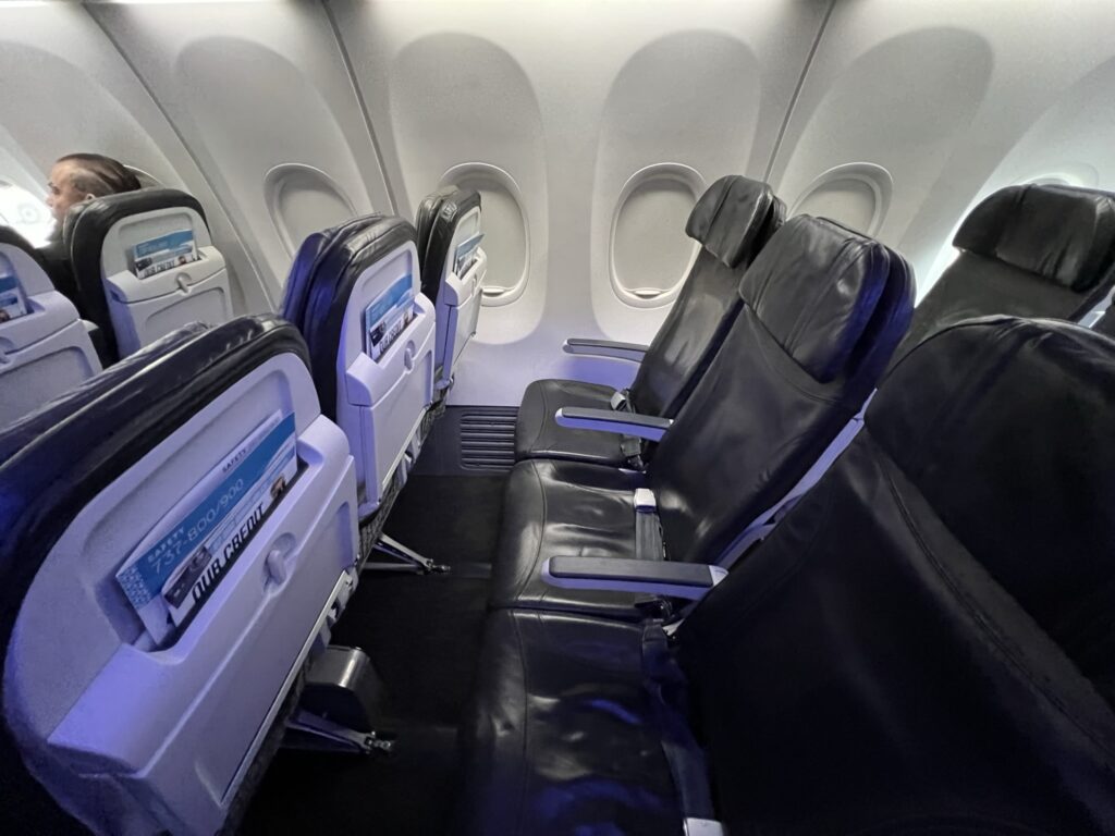 Three economy class seats on the Alaska Airlines Boeing 737-900ER. A large silver box can be seen in the space beneath the middle seat