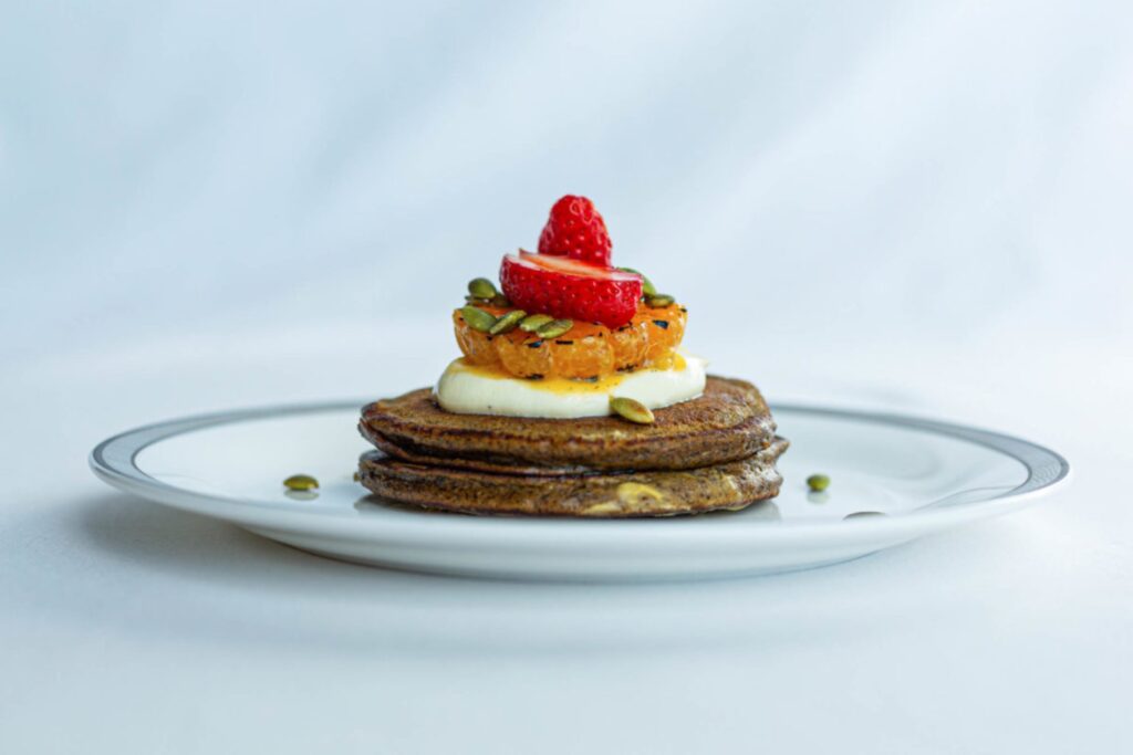 A stack of two pancakes is topped with cream, fruit and nuts.