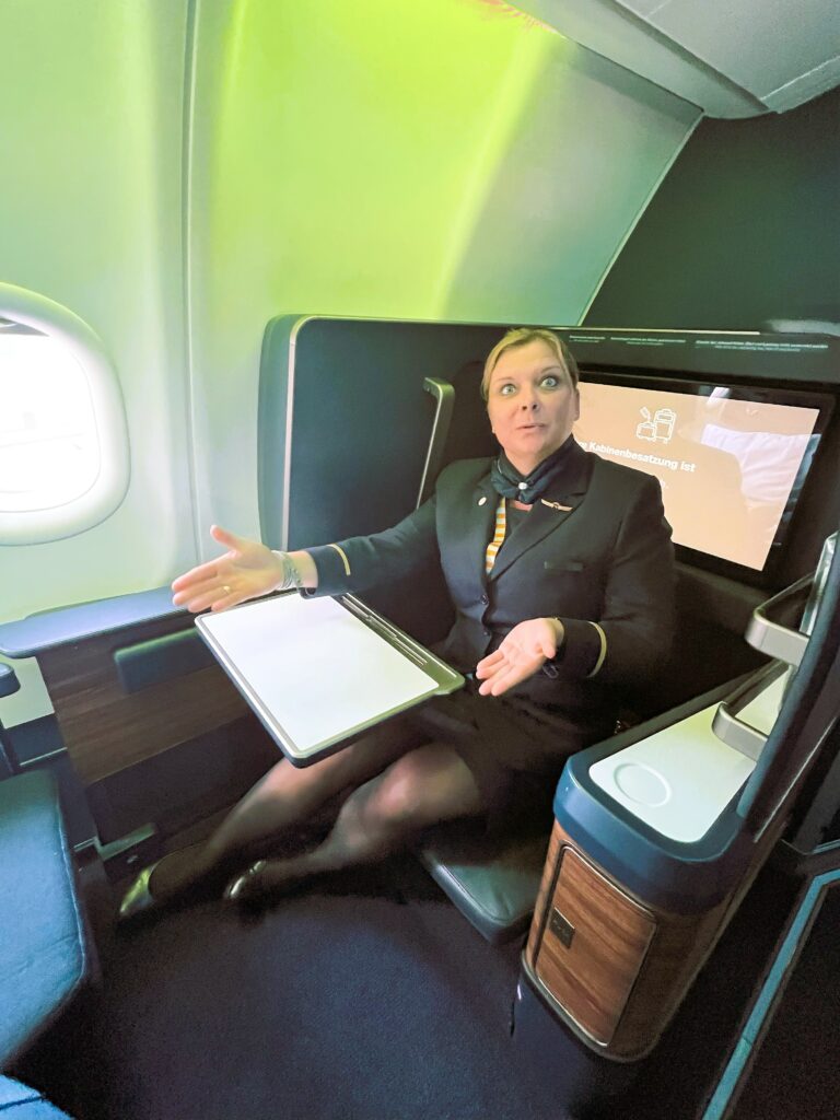 A Condor flight crew member is sitting in the business class seat, showcasing the ample space and large table.