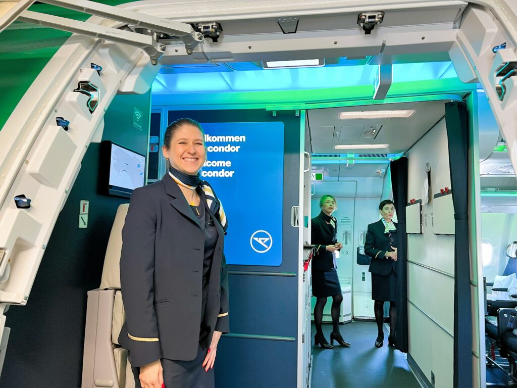 A flight attendant stands at the aircraft door to welcome guests onto the flight.