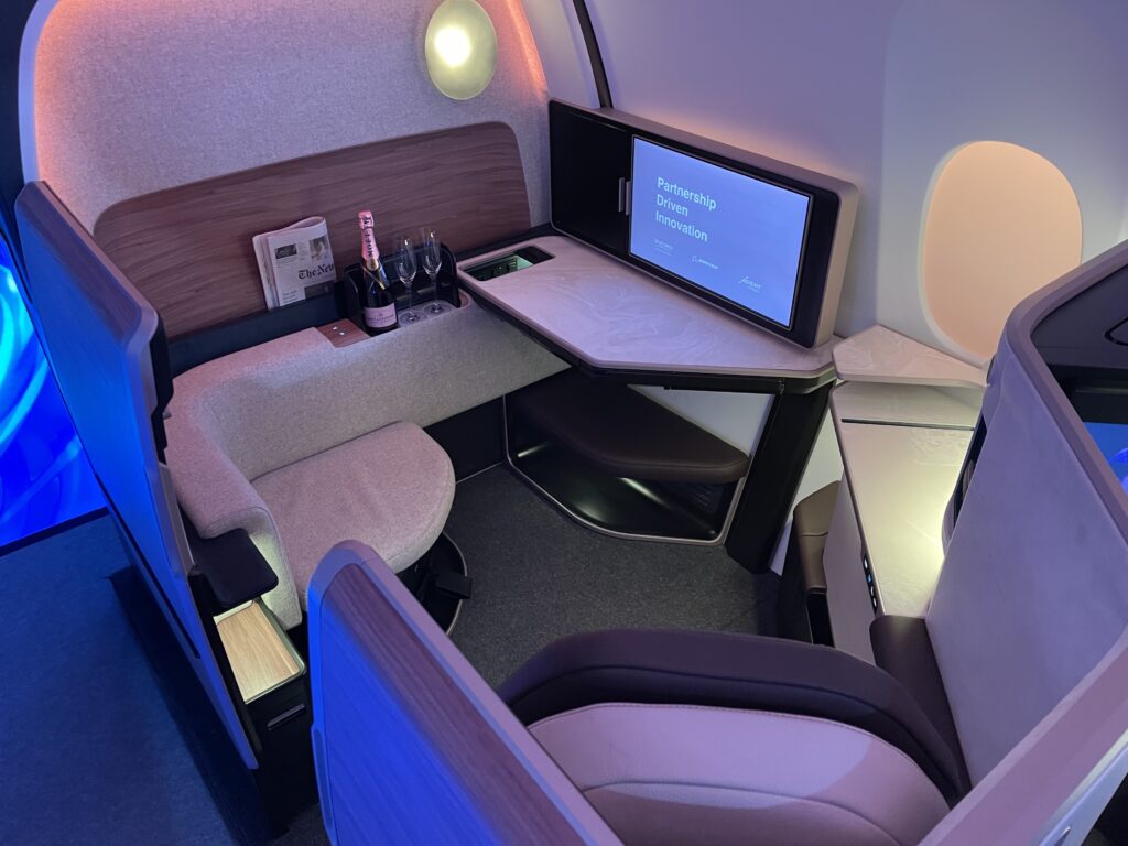 Front row business class seat in grey with purple and blue LED lighting. The space is ample, offering room to position oneself in various ways.