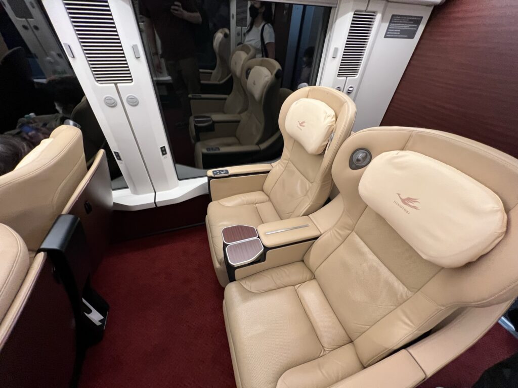 The Hinotori Limited Express premium cabin features red walls and carpet, and large cream colored seats.