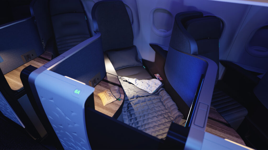 JetBlue's business class mini suite, with the seat in full-flat mode, with blue LED lighting casting a calm glow. An amenity kit sits on the table beside the bed.