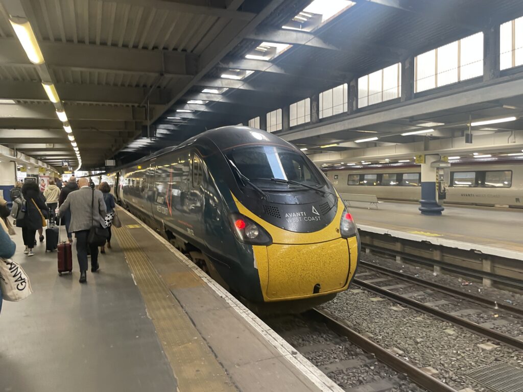 Avanti West Coast train coming into the station. The livery is black and yellow.