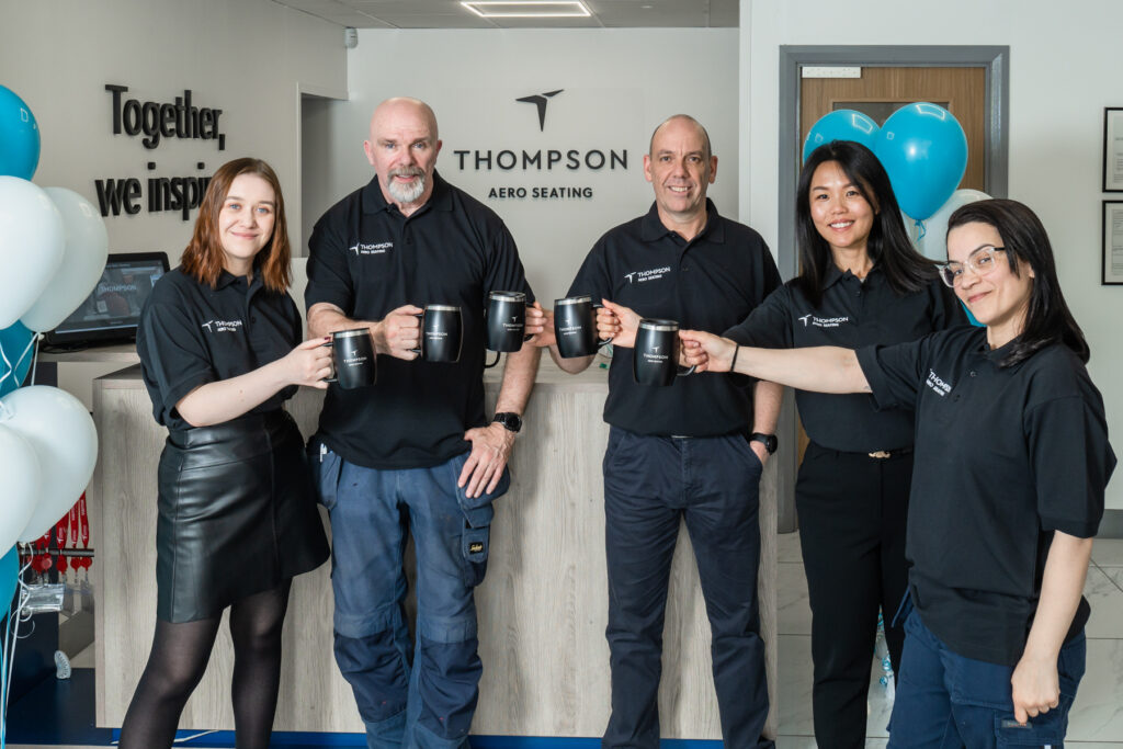 A group of Thompson Aero employees are holding up mugs with the new logo.