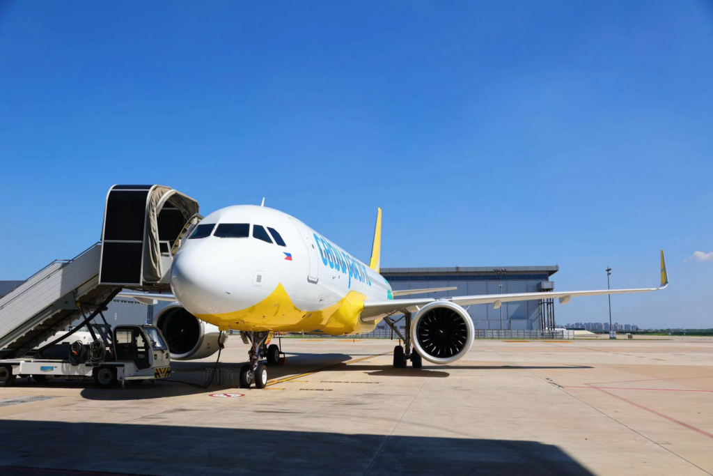 Seen parked at a stand on a blue sky day, the Cebu Pacific A320neo is all white with a yellow tail and yellow and teal lines down the belly of the aircraft.