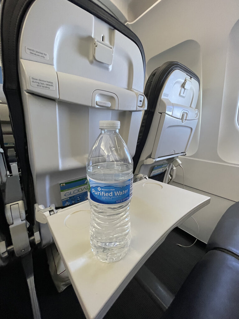 A water bottle is sitting on the Red Way aircraft tray table.
