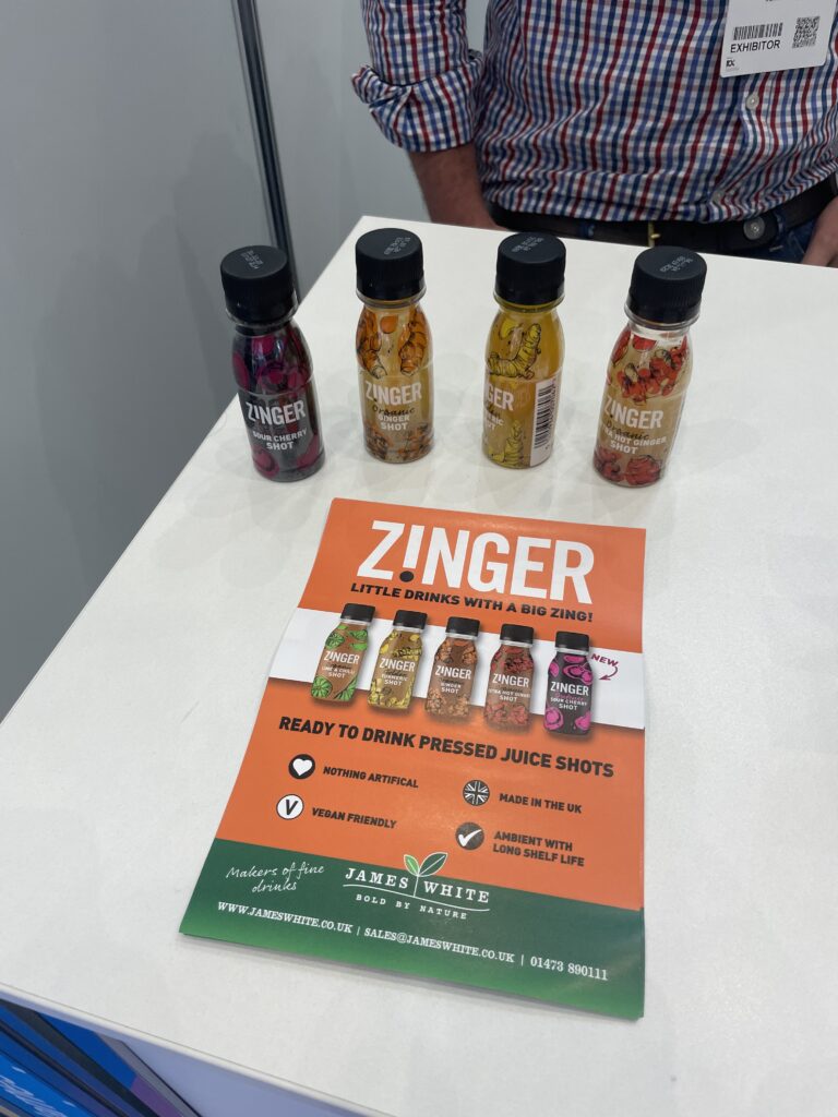 Four small Zinger shot bottles lined up on a white table, with a brochure about the product, as seen at the WTCE Exhibition. 