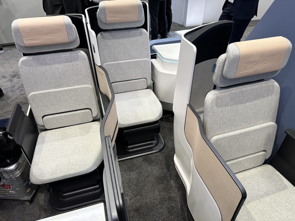 A display concept model of the C Suite by Airbus and Stelia. This is a business class seat in mostly grey fabrics with a beige headrest cover and sidewall detailing. This is a set of 3 showing the staggered layout.