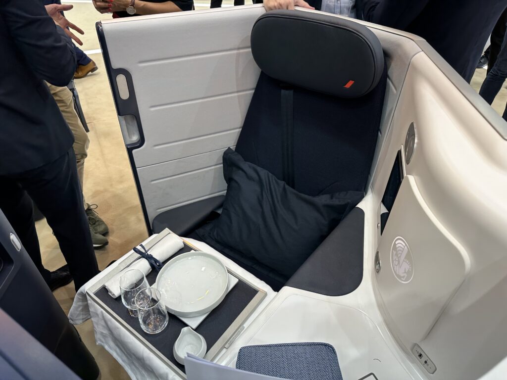 Air France's Opera seat on the show floor at AIX 2023. The large business class set is dark blue with lighter and darker thermoplastics shrouding it. A meal table is set up for dining.