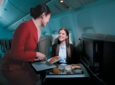 A Cathay Pacific flight crew member is serving a female business class passenger her meal. coffin