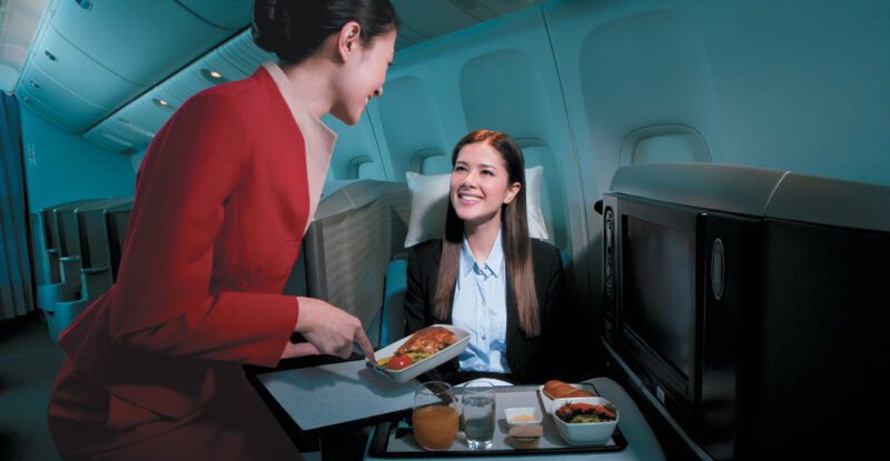 A Cathay Pacific flight crew member is serving a female business class passenger her meal. coffin