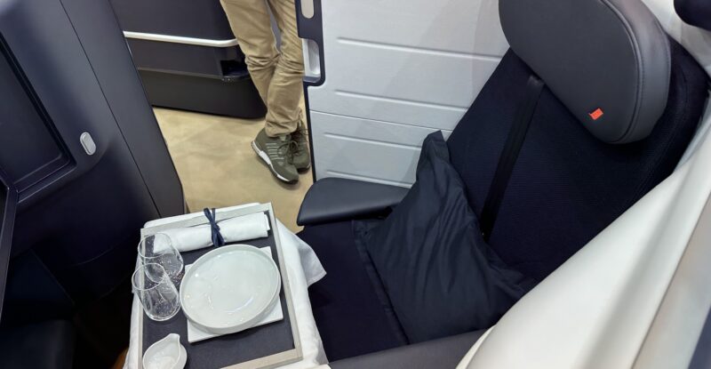 Air France's Opera seat by Stelia on the show floor at AIX 2023. The large business class seat is dark blue with lighter and darker thermoplastics around it.