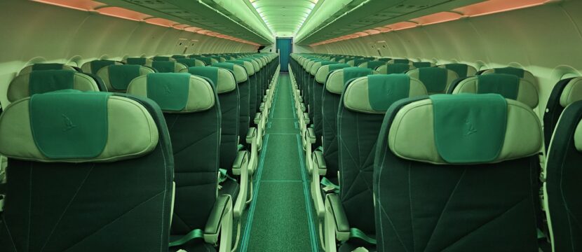 Green LED lighting is casting into a cabin that is configured in a 2-2 layout. There is a red light strip down the sides of the aircraft.
