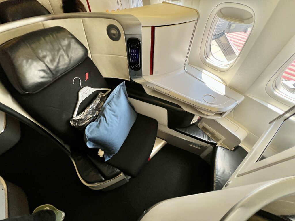 Business class seat on board the Air France 777, with a blue pillow and a hangar waiting on the seat for the passenger.