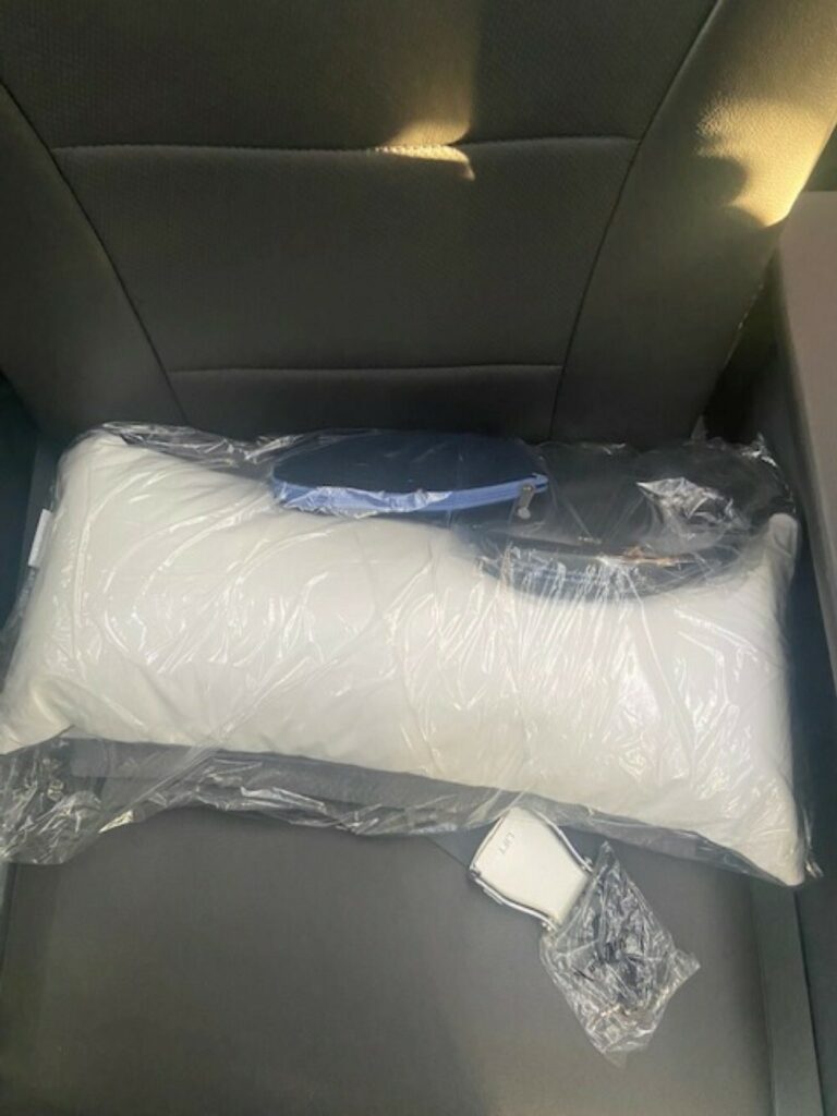 An amenity kit, ear plugs and a white pillow are displayed on the American Airlines premium economy 787 seat.