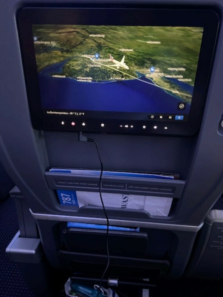 Headphones are plugged into the seatback IFE as it displays the moving map and details of the flgiht.