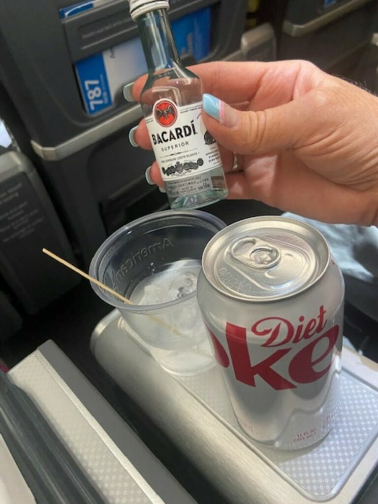 A passenger is holding up a mini bottle of rum next to a can of Diet Coke.