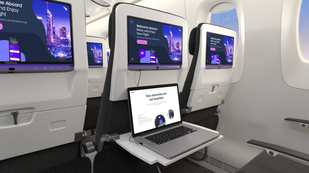 Panasonic's Astrova IFE in an economy class seat triple. A laptop is sitting on a tray table, being fully charged by the IFE's USB-C port.