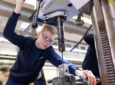 A female Lufthansa Technik (LHT) machinist is working with a tool.