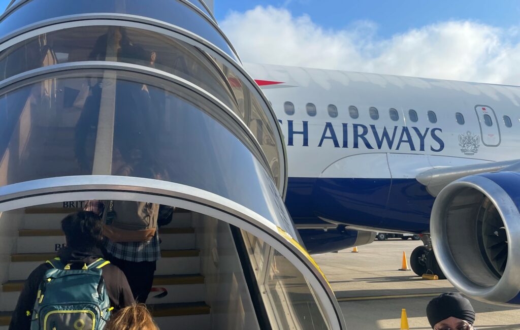 Passengers are boarding the British Airways (BA) A319 via glass-enclosed stairs in the early morning hours.