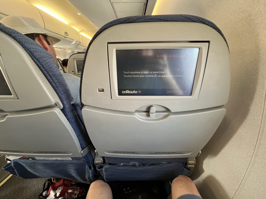 The author's legs are in view, whilst he is seated in the E175. His reflection can be seen in the IFE screen.