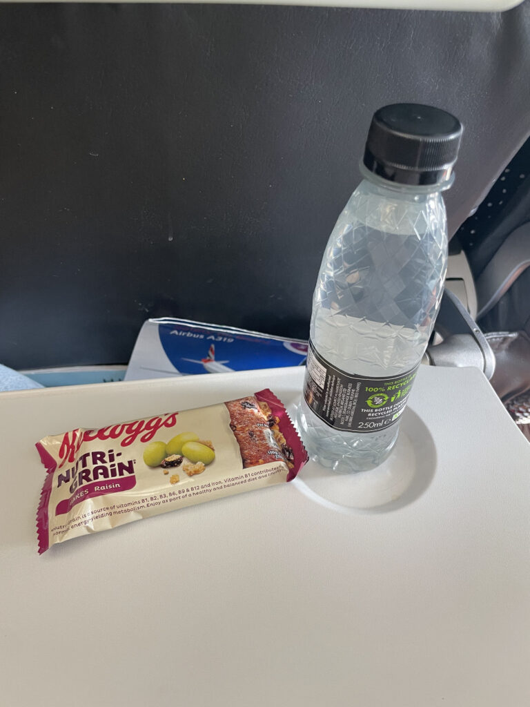 A breakfast bar and a bottle of water sit on the BA tray table. 