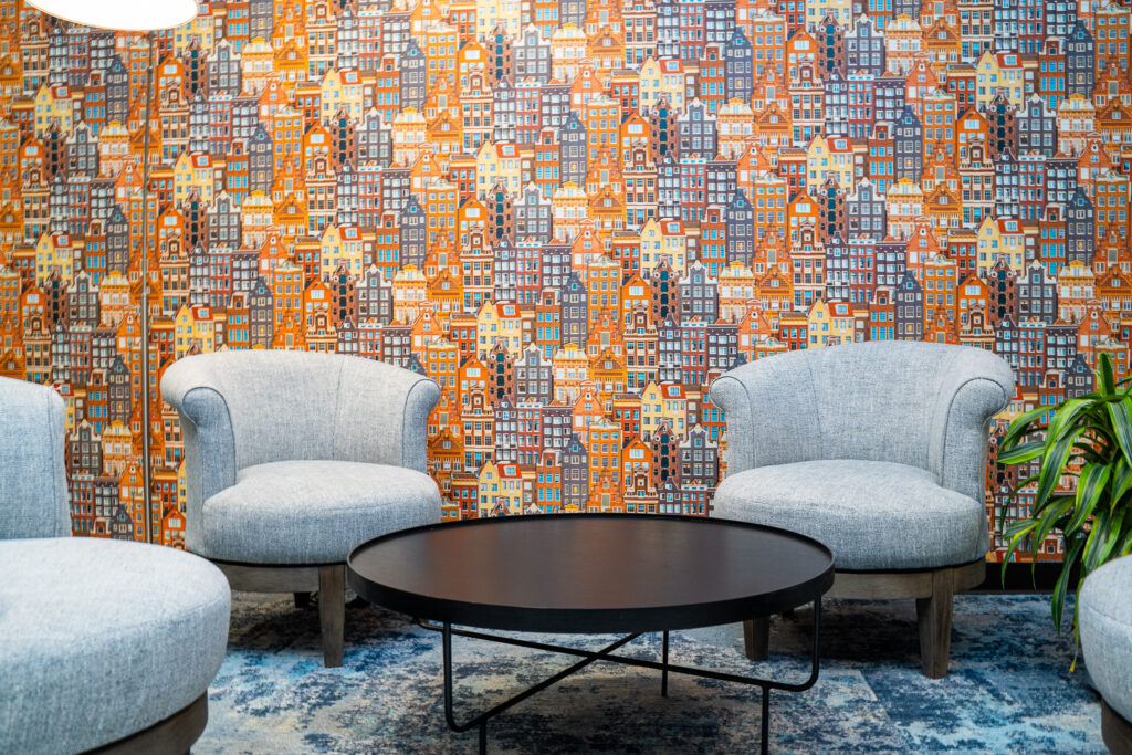 Grey chairs in the KLM Crown Lounge in Houston, flanked by a large colorful wall made up of pictures of Dutch houses. 