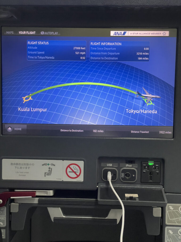 Power ports under the embedded IFE screen. The screen shows a moving map with Tokyo Haneda listed as the destination. 