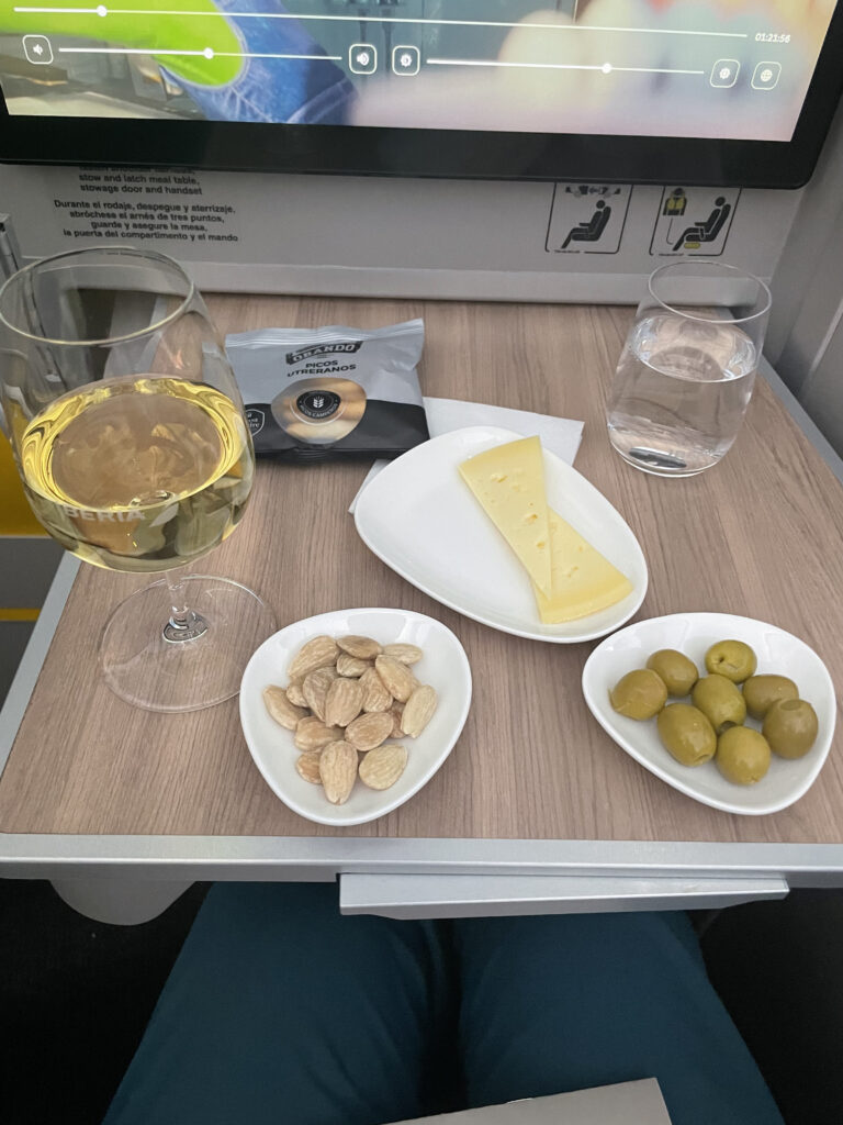 A display of various snacks and drinks on the aircraft table, including Spanish favorites like olives and Manchego cheese.