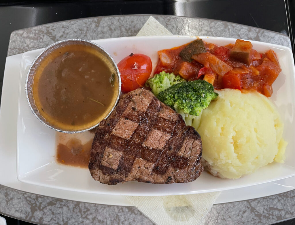 An impressive looking main meal with a succulent steak, a side of mashed potatoes and vegetables and a gravy for the steak.