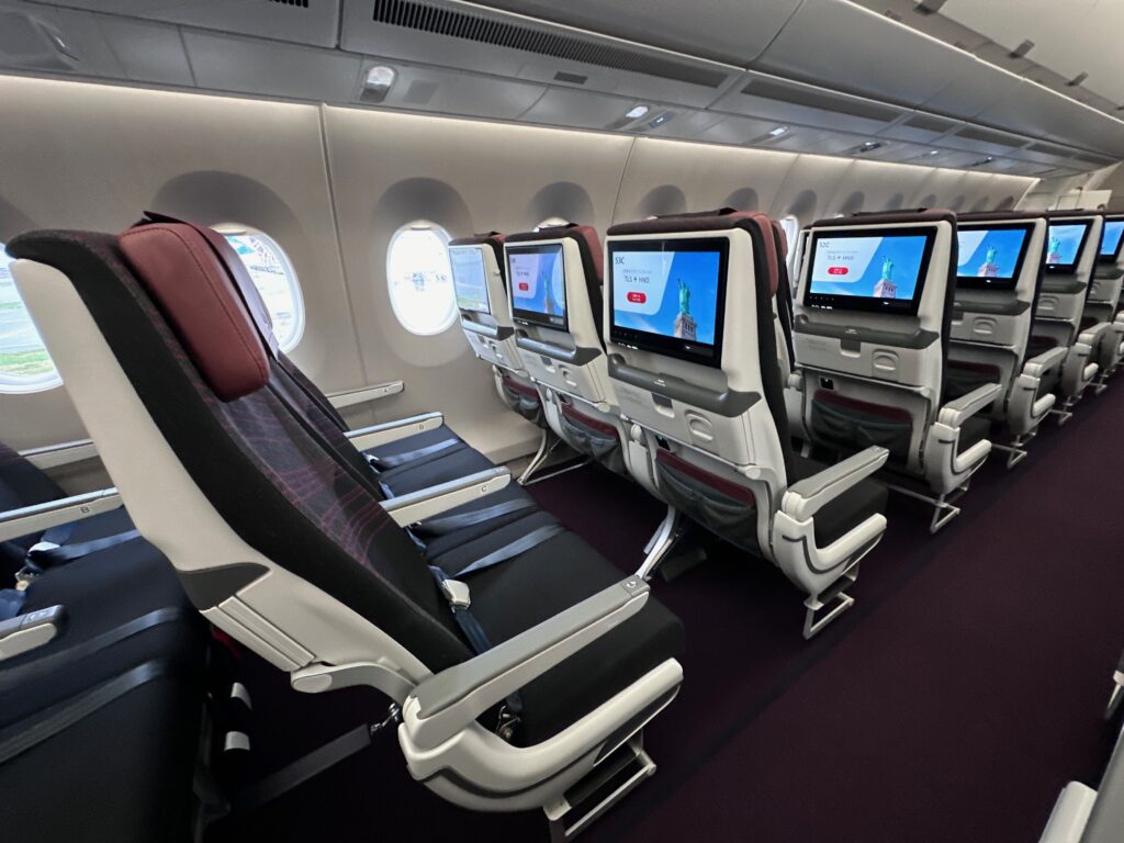 JAL economy class seat triples near the windows. Large IFE screens are in view.