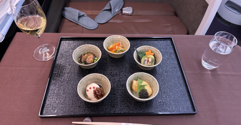 Five bowls with various Japanese dishes and chopsticks are laid out on the first class tray table.