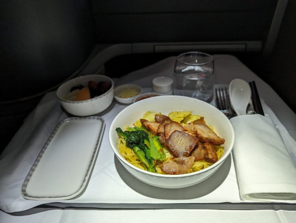 Pork dumpling noodle dish from Singapore Airlines' Book the Cook menu displayed in white dishware on an aircraft tray table.