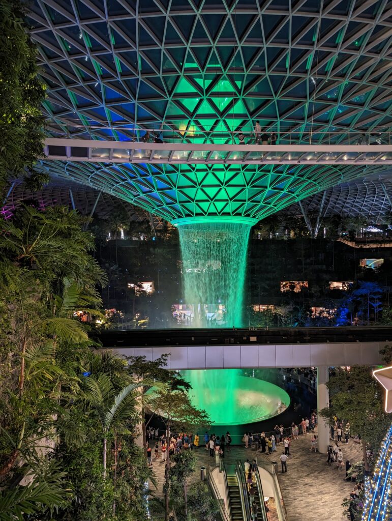 A massive waterfall inside the Jewel Mall at Singapore Changi International Airport is illuminated with green and blue LED lights. It's a very visually impressive structure.