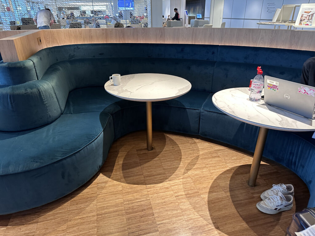 A large blue cushioned bench with small white round tables.