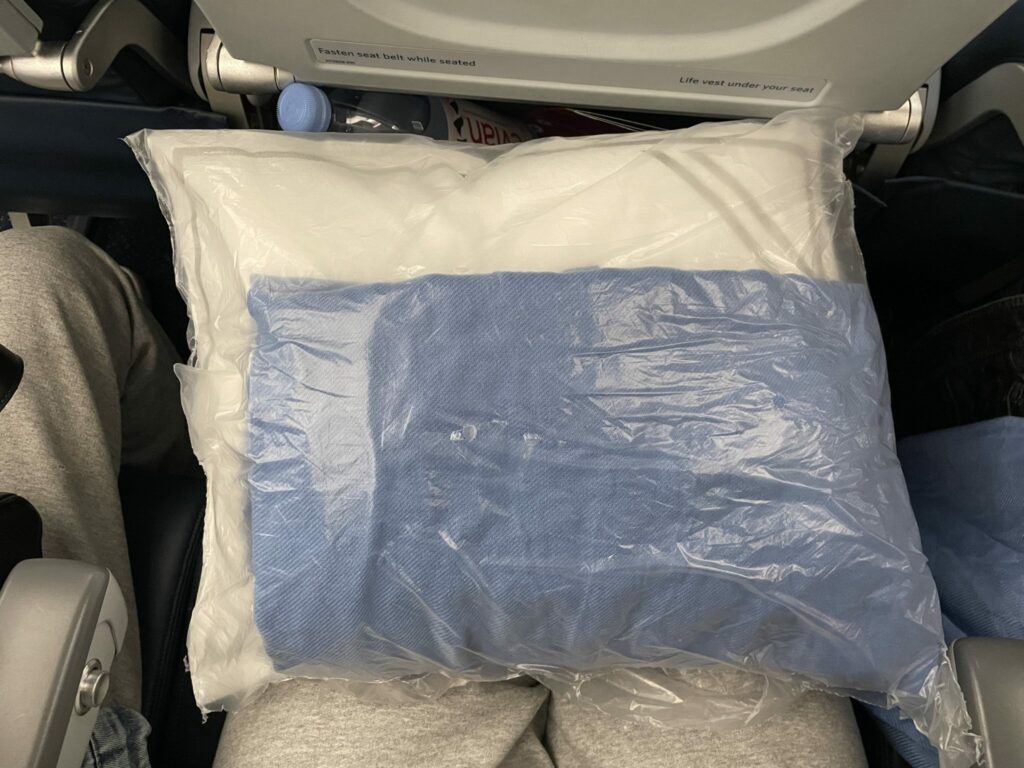 A small blue blanket and white pillow are wrapped in plastic for economy class passengers.