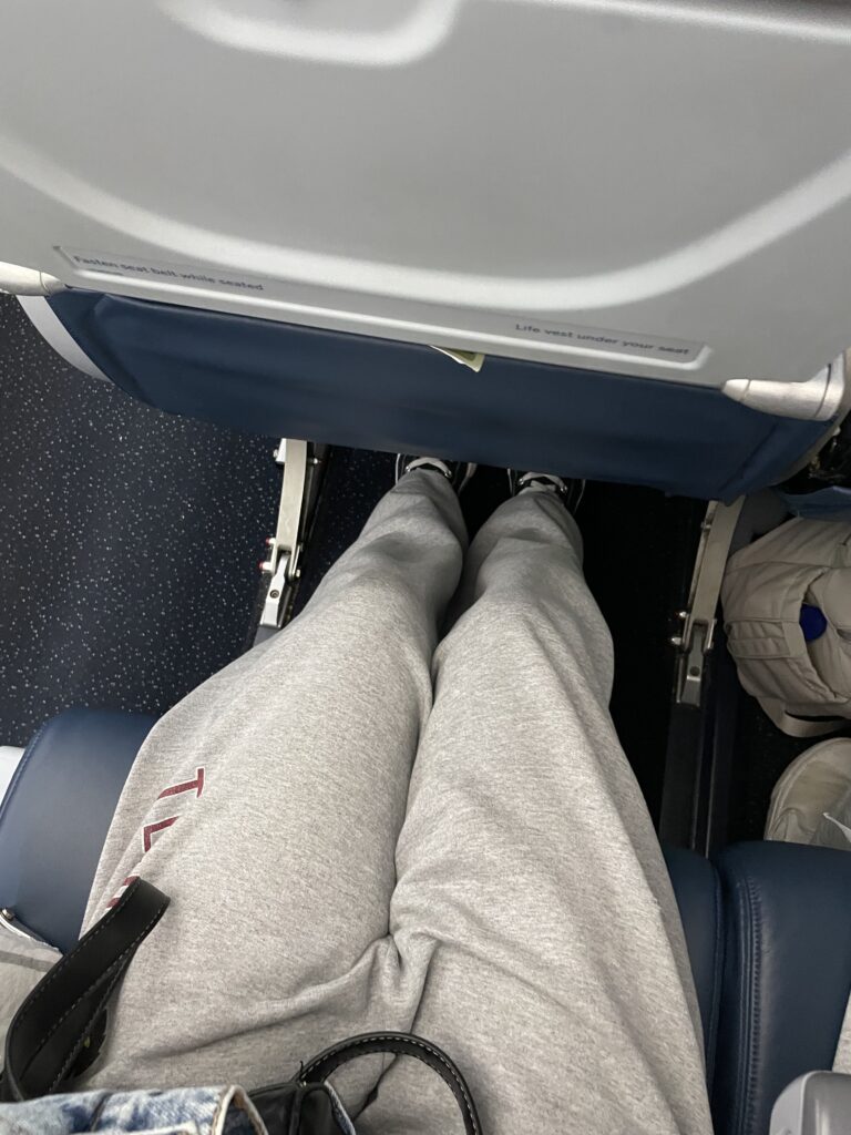 A petite passenger's legs are pictured stretched out underneath the seat in front of her on a Delta flight. 